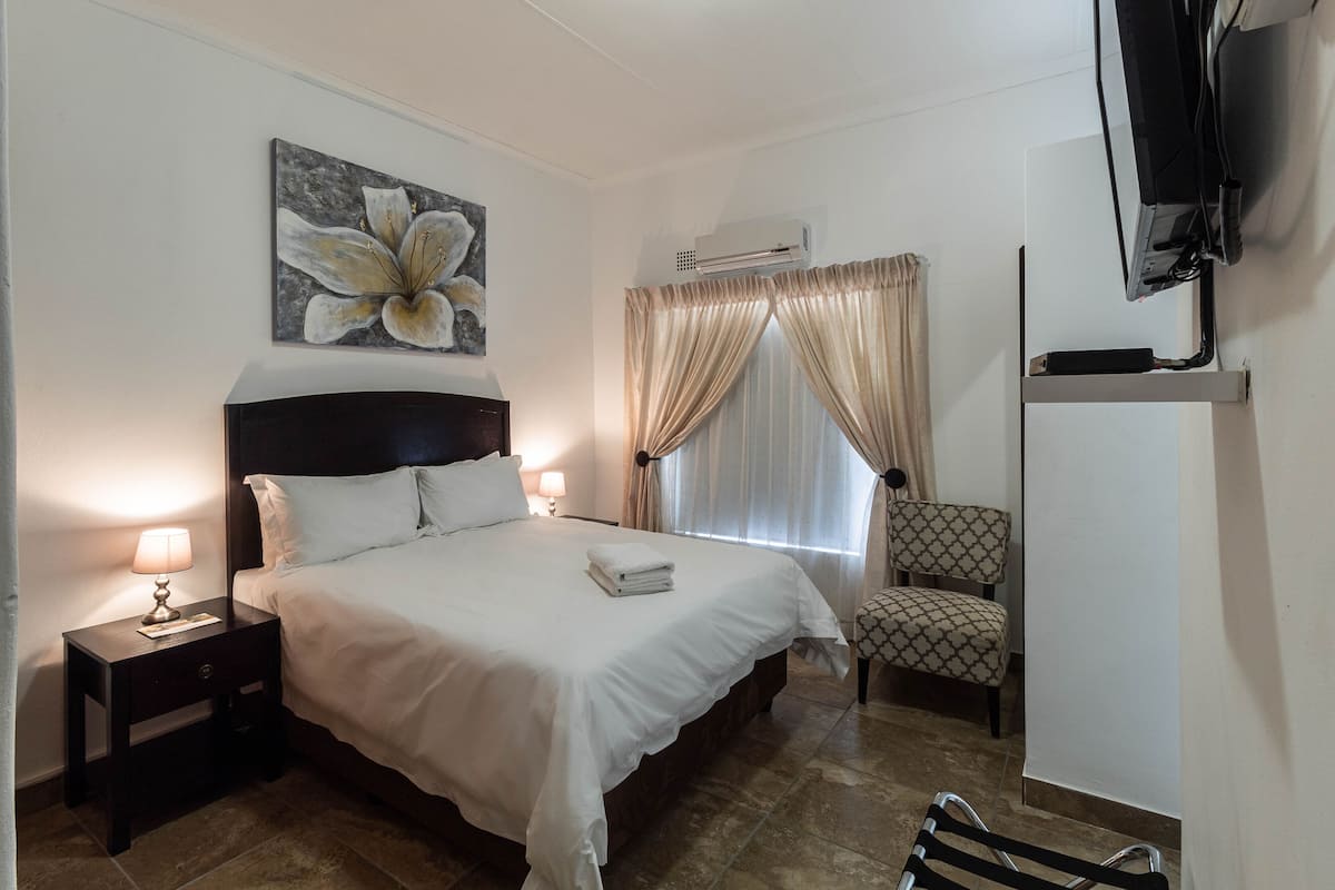 Un dormitorio ordenado con cama, una silla, un televisor y un equipo de aire acondicionado.