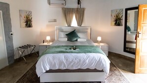 A bedroom with a bed, two bedside tables, a mirror, a window with curtains, and a wall-mounted air conditioner. - Graceland Conference & Lifestyle Centre (Akasia)