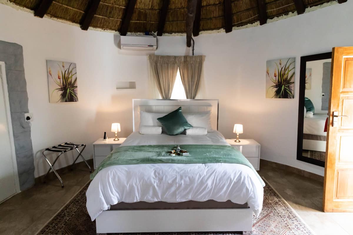 Un dormitorio con cama, dos mesitas de noche, un espejo, una ventana con cortinas y aire acondicionado instalado en la pared.