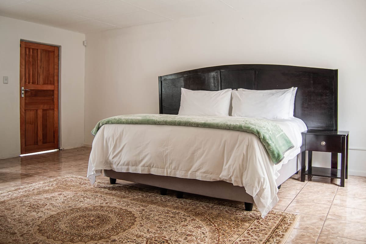Un dormitorio con cama, mesita de noche, puerta de madera y alfombra estampada.