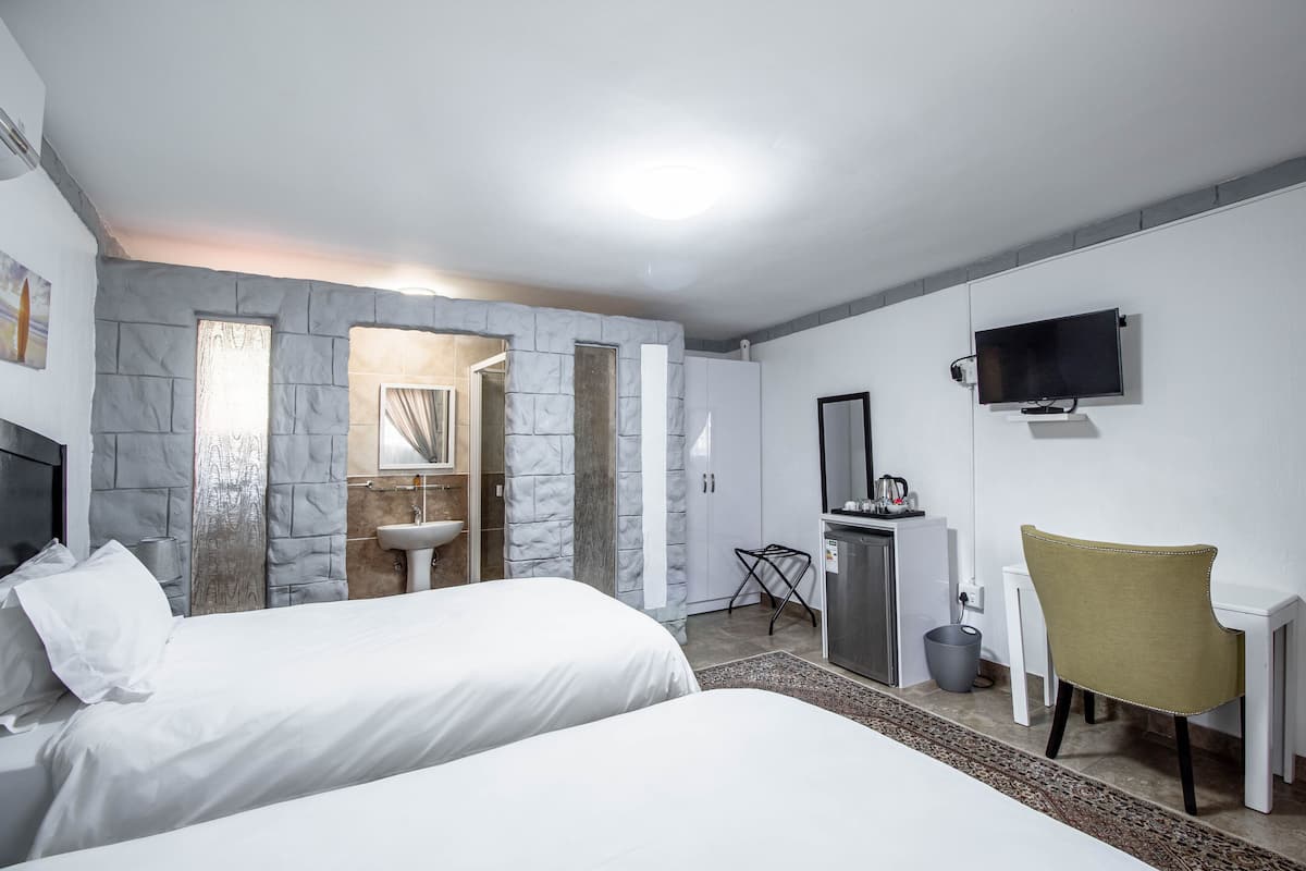 Habitación de hotel con dos camas, un escritorio, una silla, un televisor y un baño con pared de piedra.