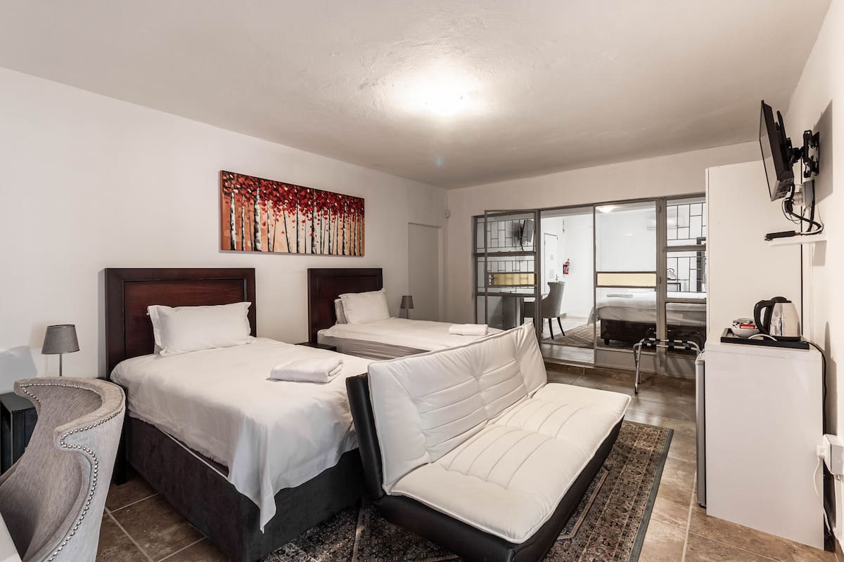 Habitación de hotel con dos camas, un sofá, un escritorio, una silla, un televisor y un cuadro en la pared.