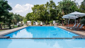 A rectangular swimming pool with a clear blue water surface, surrounded by trees and a lounge area with sun loungers and an umbrella. - Graceland Conference & Lifestyle Centre (Akasia)