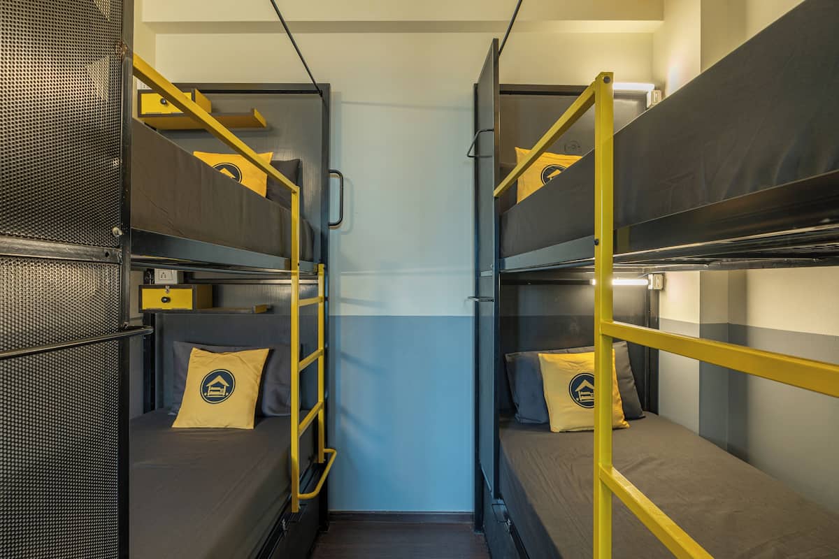 A compact, well-lit room with bunk beds and a small desk area, featuring a simple, functional design.