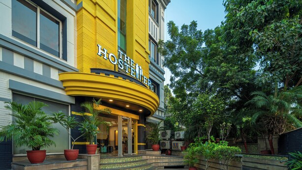 A hotel entrance with a curved yellow facade, steps leading up to the entrance, and potted plants around the area. - The Hosteller Delhi (New Delhi)