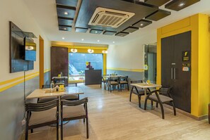 A restaurant with a bar area, tables, chairs, and a view through a large window. - The Hosteller Delhi (New Delhi)