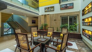 A spacious lobby with a high ceiling, a staircase, and a seating area with a chess table. - The Hosteller Delhi (New Delhi)