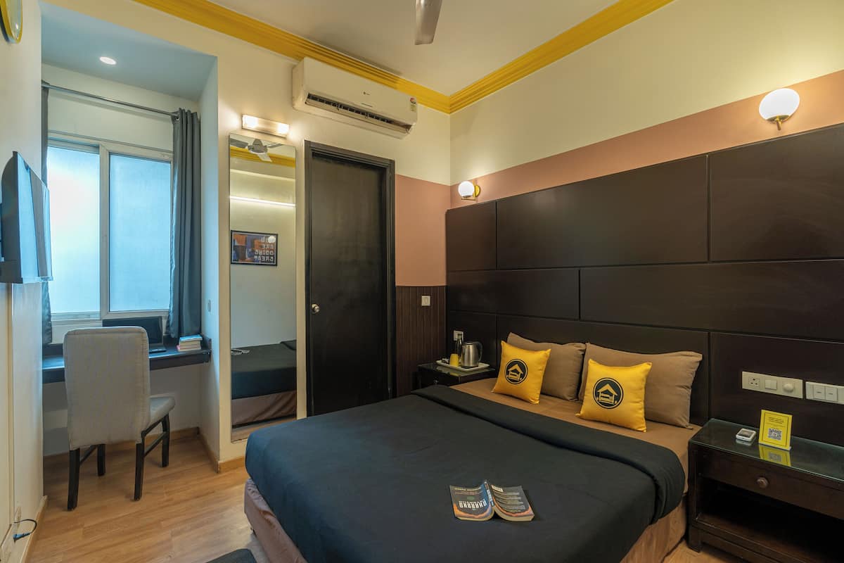 A hotel room with a bed, a desk, a chair, a nightstand, and a window.