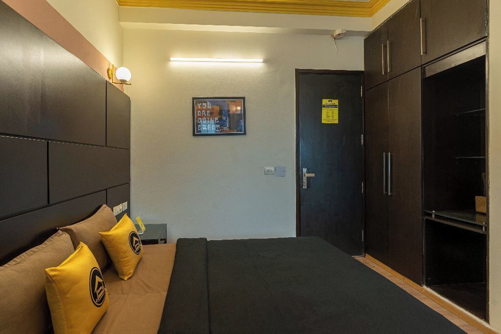 A hotel room with a bed, a wardrobe, a nightstand, and a wall-mounted light fixture.