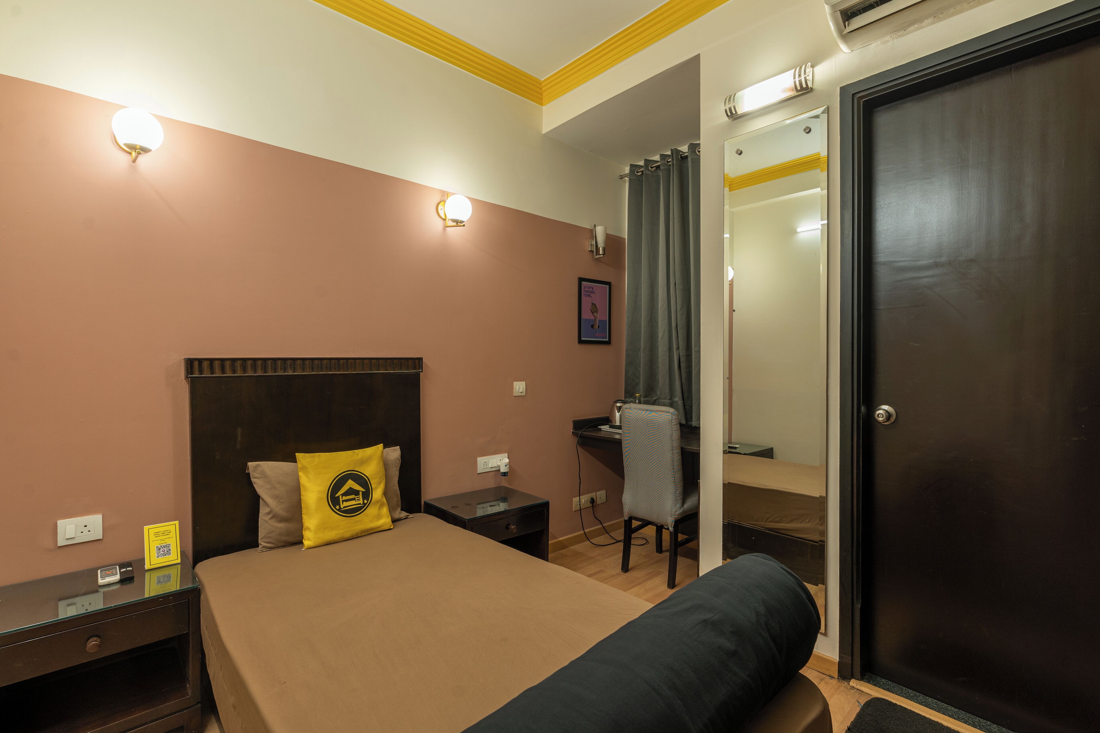 A hotel room with a bed, a desk, a chair, a nightstand, and a door.