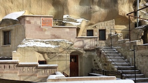 Ein Steingebäude mit einem Schild für das Monastery Cave Hotel. Es führen Treppen zu einer Tür, und es gibt eine Treppe mit Geländern.