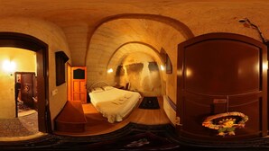 Ein schmaler, gewölbter Raum mit einem Bett, einer Sitzbank und einer Tür zu einem weiteren Zimmer.