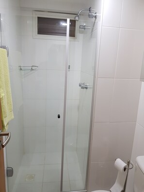 A glass-enclosed shower stall with a towel rack and a small window above. - Apartamento na praia de Armação. (Salvador)