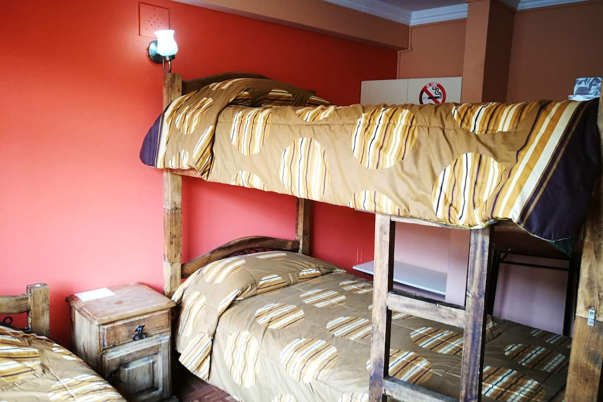 A bunk bed with striped bedding, a bedside table, and a wall-mounted light fixture.