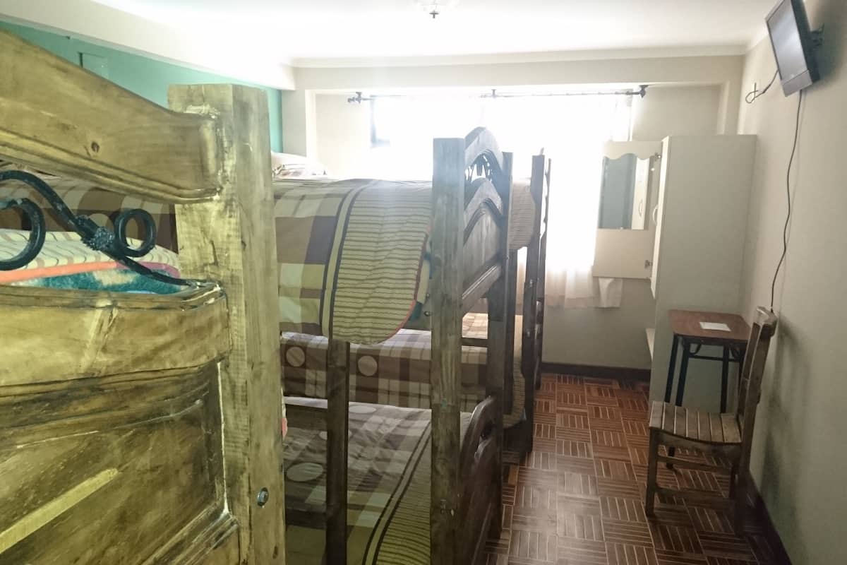 A room with a wooden bed frame, a checkered bedspread, a small table, and a mirror on the wall.
