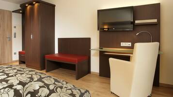 A modern hotel room with a bed, a desk, a chair, a TV, and a wardrobe.