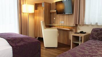 A hotel room with two beds, a desk, a television, and a lamp.