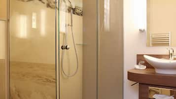 A modern bathroom with a glass-enclosed shower, a wooden vanity, and a marble backsplash.