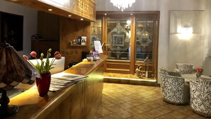 A reception area with a wooden reception desk, a chandelier, patterned chairs, and a glass display case. - Hotel Simonshof Wolfsburg (Wolfsburg)
