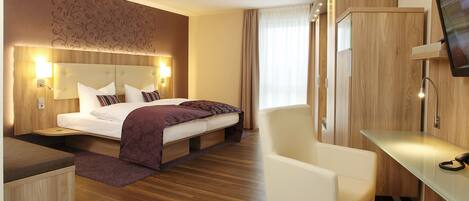 A modern hotel room with a large bed, a desk, a chair, and a TV mounted on the wall.