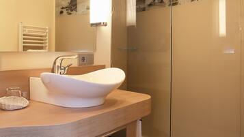 A modern bathroom with a large mirror, a white sink, a glass shower enclosure, and wooden flooring.