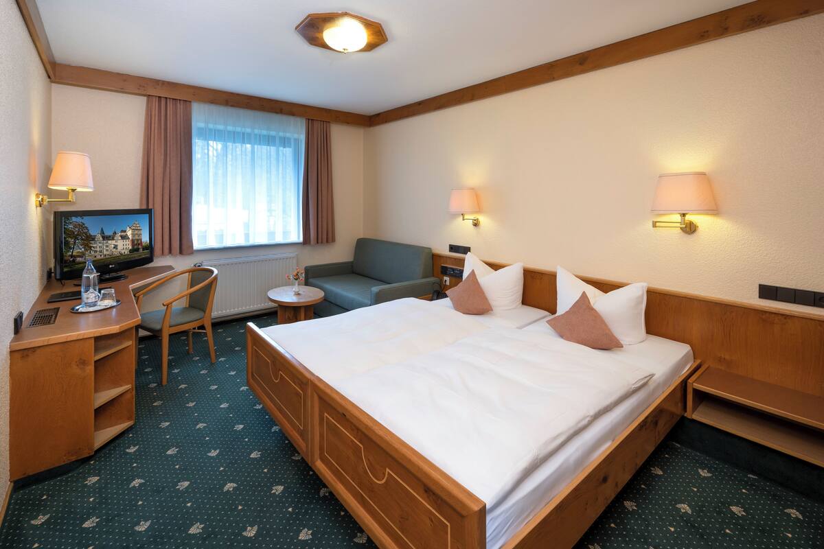 Habitación de hotel con una cama grande, un escritorio con computadora, una silla, una mesita redonda y dos lámparas fijadas a la pared.