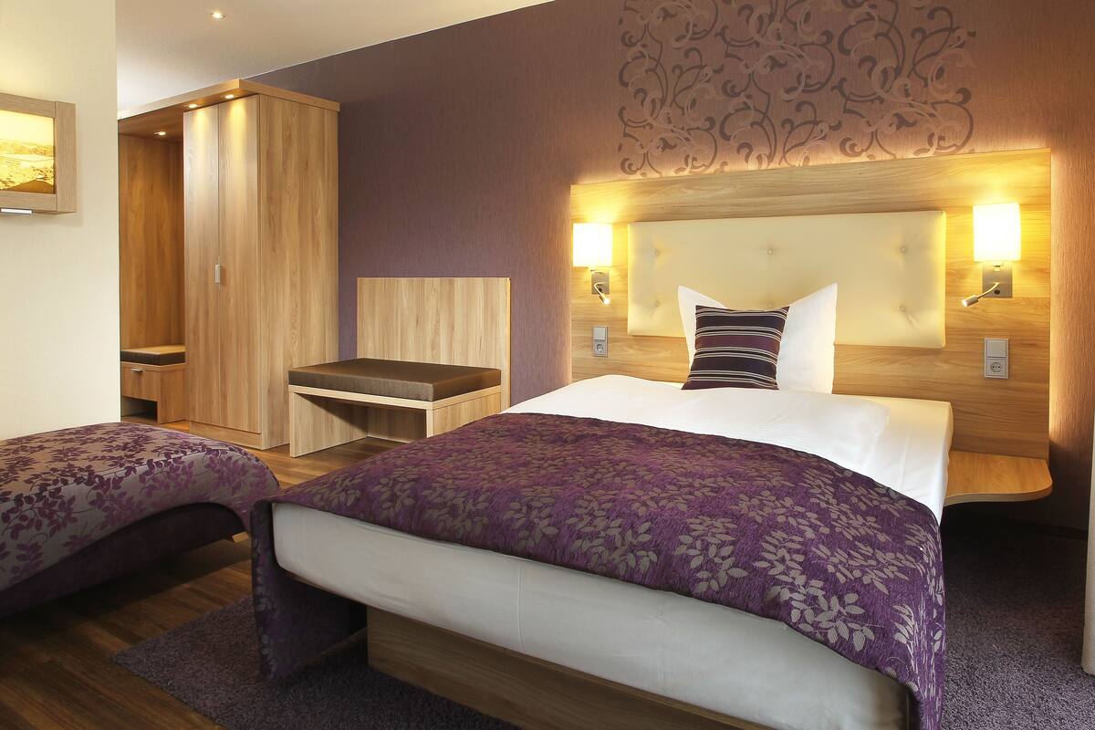 Habitación de hotel con una cama grande, dos mesitas de noche, un armario de madera y un escritorio.
