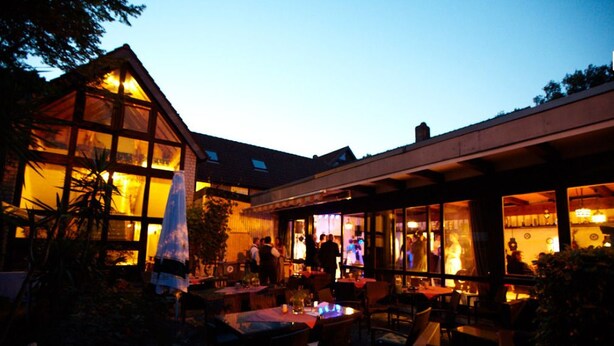 An outdoor dining area with tables and chairs, a covered seating area, and a building with large windows. - Hotel Simonshof Wolfsburg (Wolfsburg)