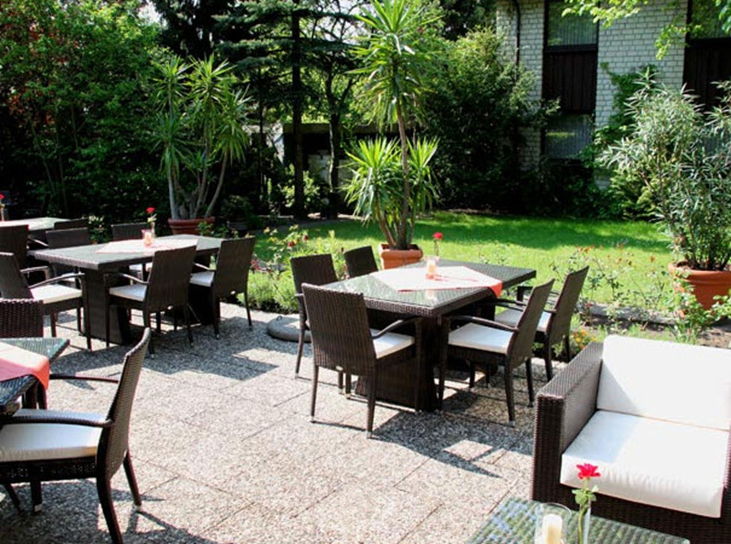 An outdoor patio area with multiple tables and chairs, surrounded by lush greenery and potted plants.