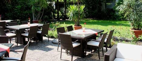 An outdoor patio area with multiple tables and chairs, surrounded by lush greenery and potted plants.