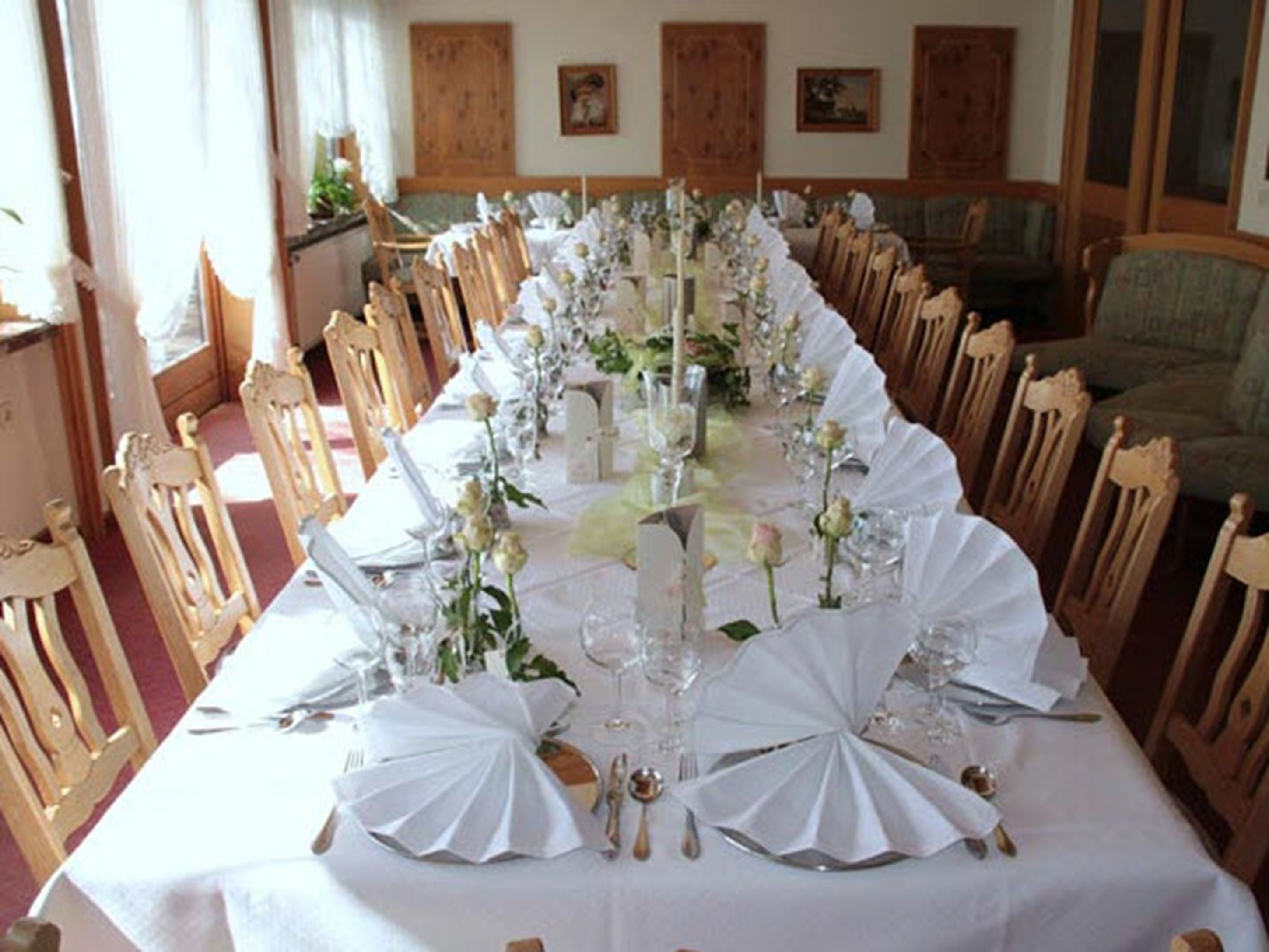 Una larga mesa de comedor con manteles blancos, centros de mesa florales y cubiertos dorados.