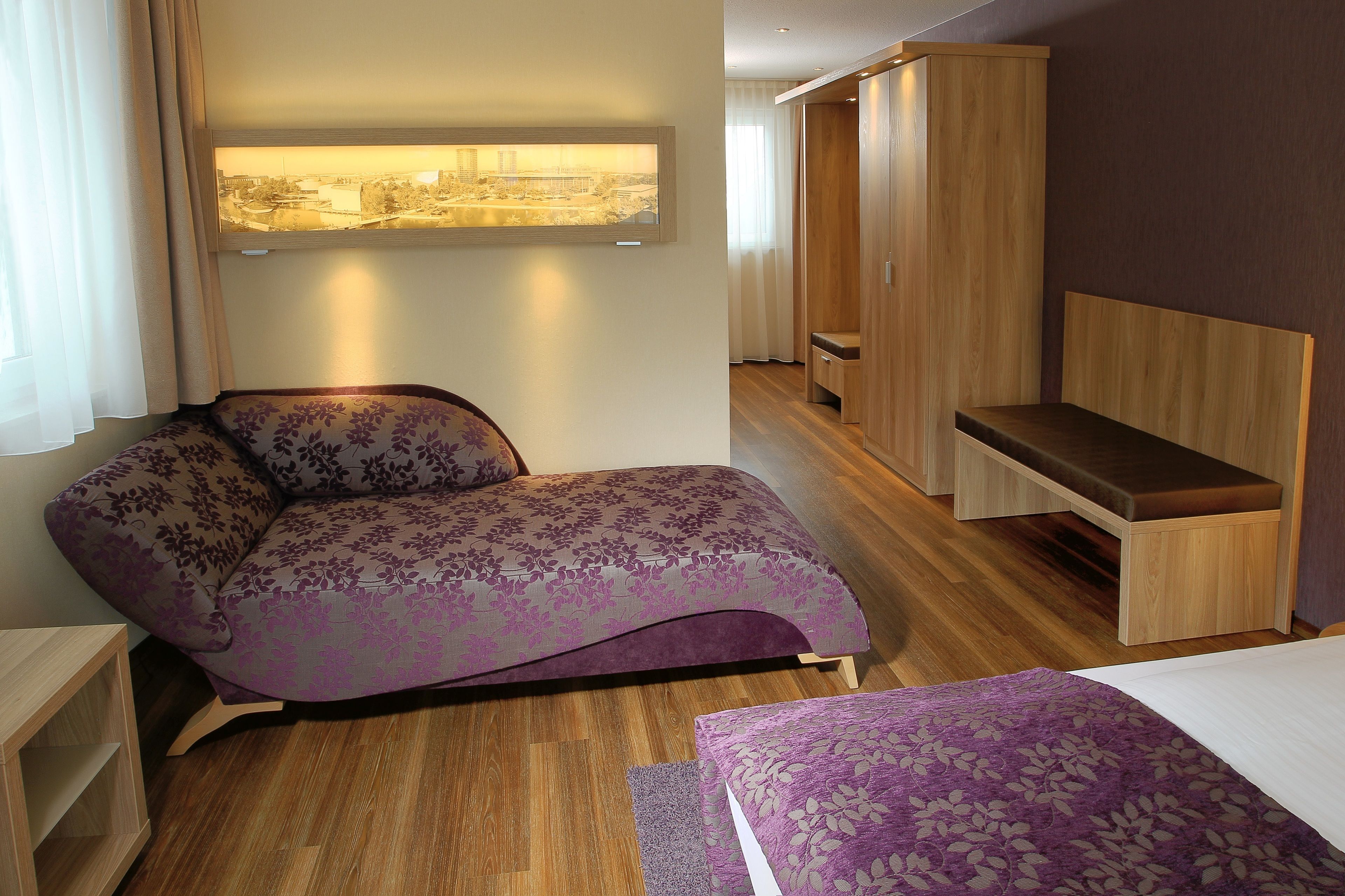A modern hotel room with a bed, a bench, and a wardrobe.