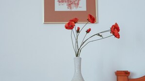 A wooden nightstand with a vase of red flowers, a framed picture on the wall, and a bed with wooden headboard. - Arthotel ANA Panorama, Trademark Collection by Wyndham (Marktoberdorf)