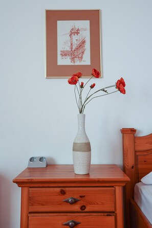A wooden nightstand with a vase of red flowers, a framed picture on the wall, and a bed with wooden headboard. - Arthotel ANA Panorama, Trademark Collection by Wyndham (Marktoberdorf)