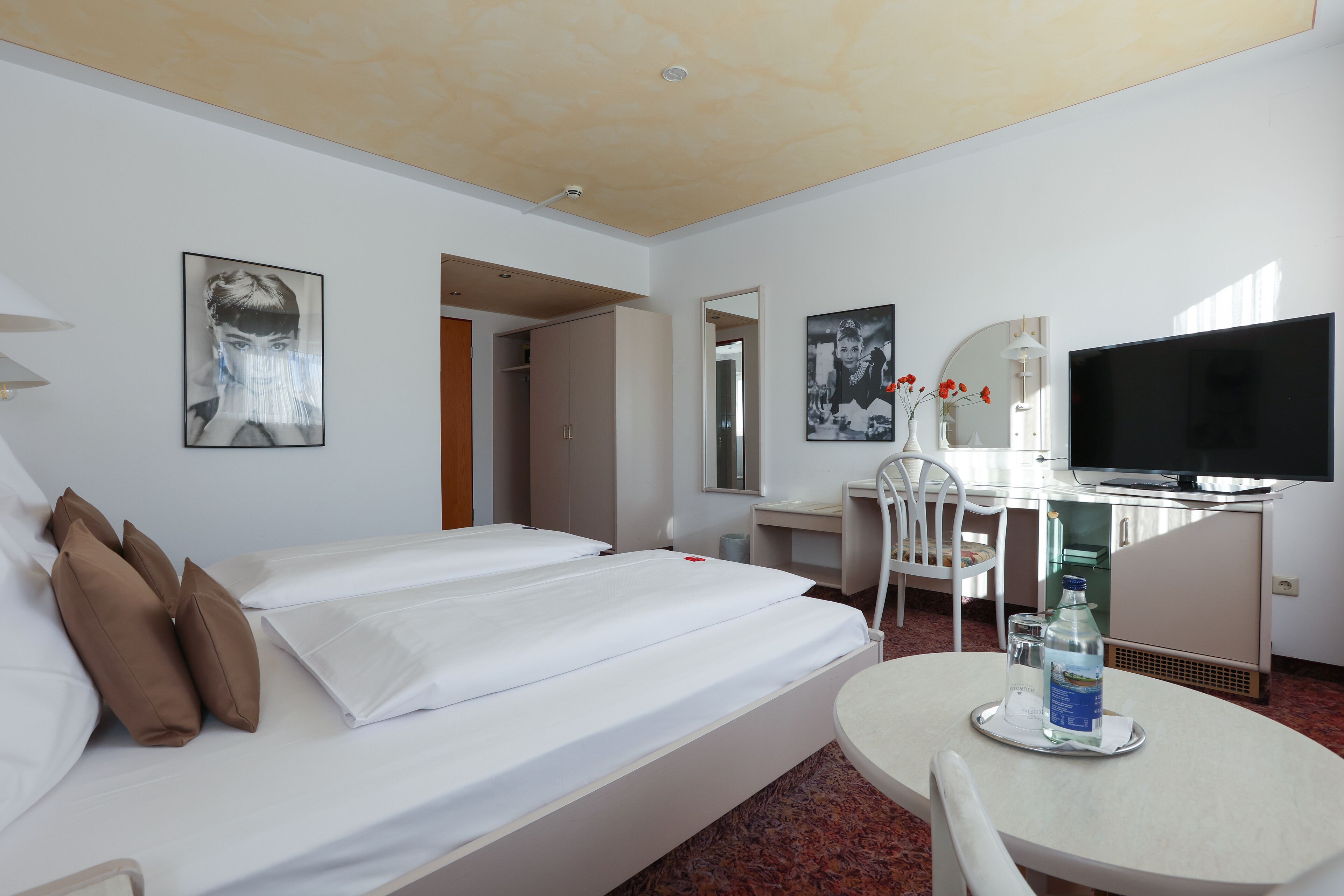 Une chambre d’hôtel avec un lit, un bureau, une chaise, une télévision et une bouteille d’eau sur la table.