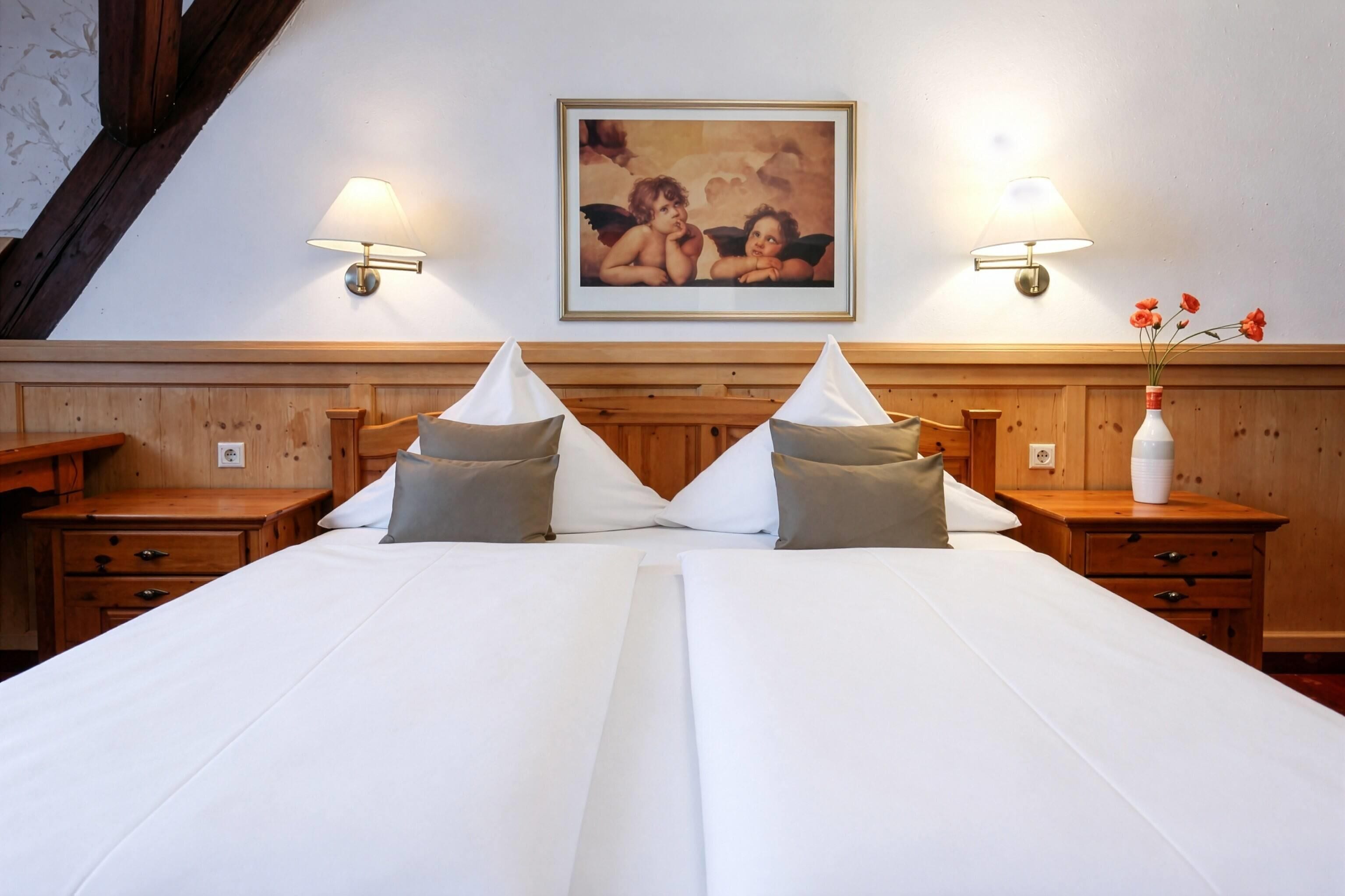 A double bed with pillows, two bedside tables, a painting above the bed, and a vase with flowers on the right table.