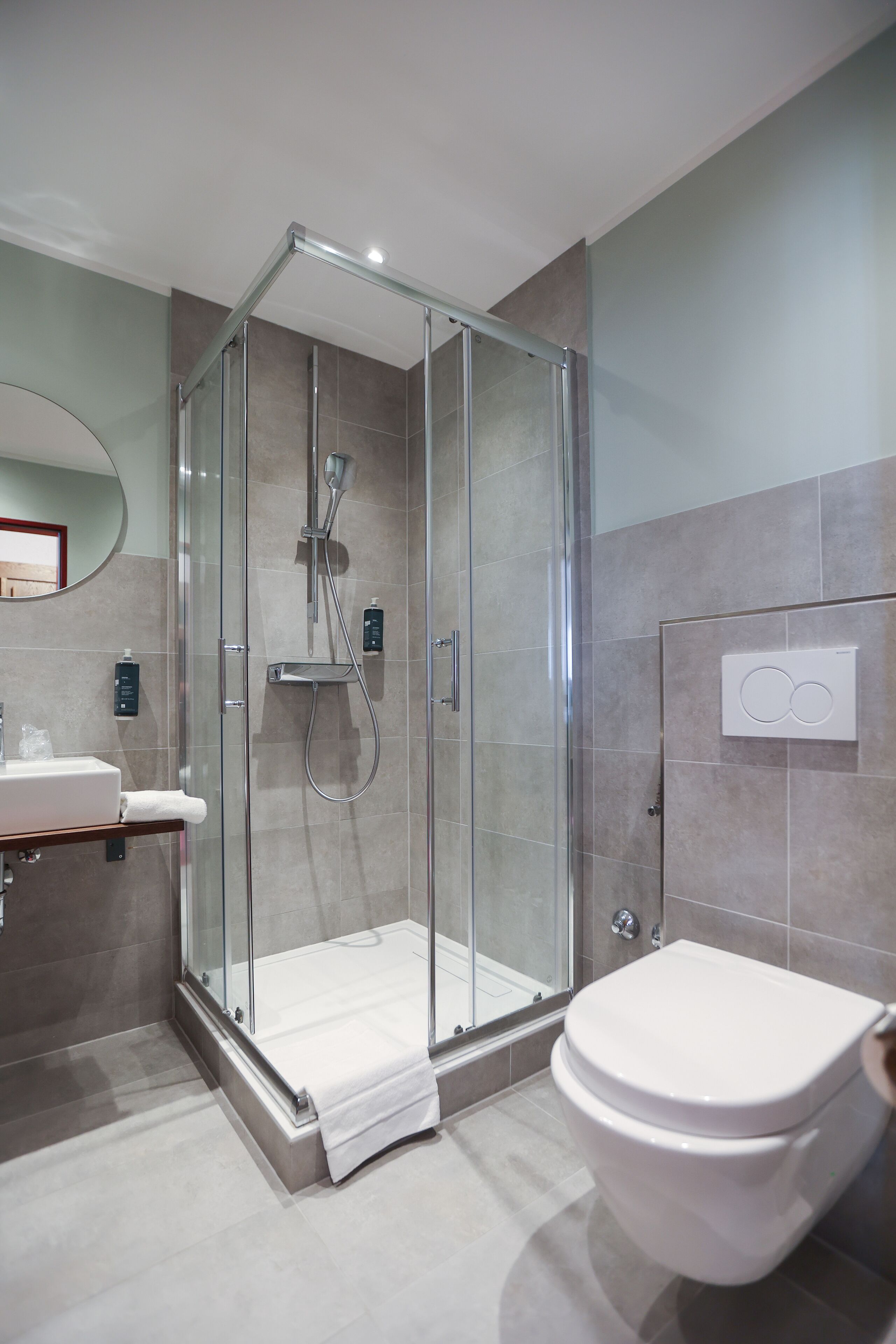 A modern bathroom with a glass-enclosed shower, a white toilet, and a sink with a mirror.