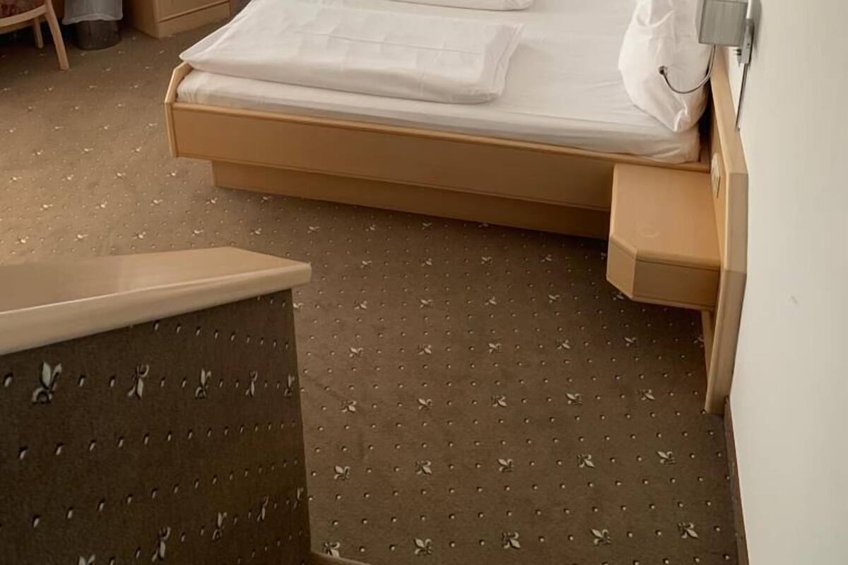A hotel room with a bed, a desk, a television, a painting, and a wall-mounted light.