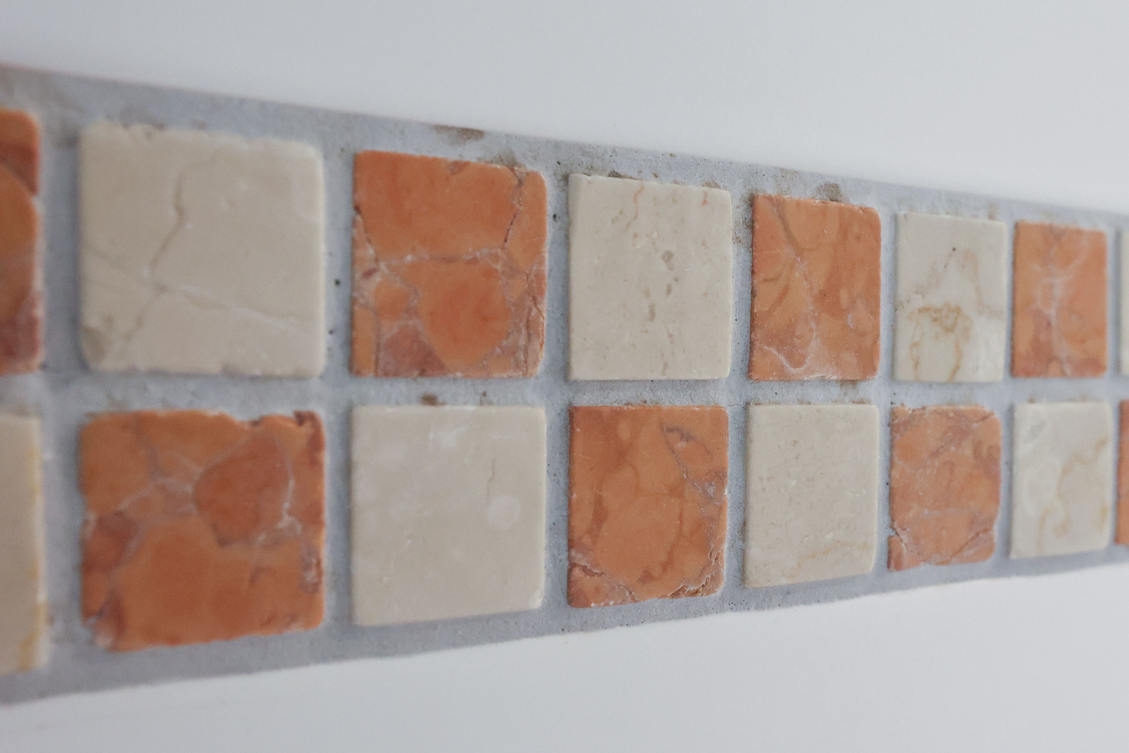 Una pared con un diseño de baldosas cuadradas en varios tonos de beige y naranja.
