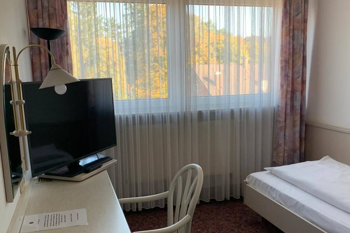 A hotel room with a bed, a desk with a computer, a chair, and a window with curtains.