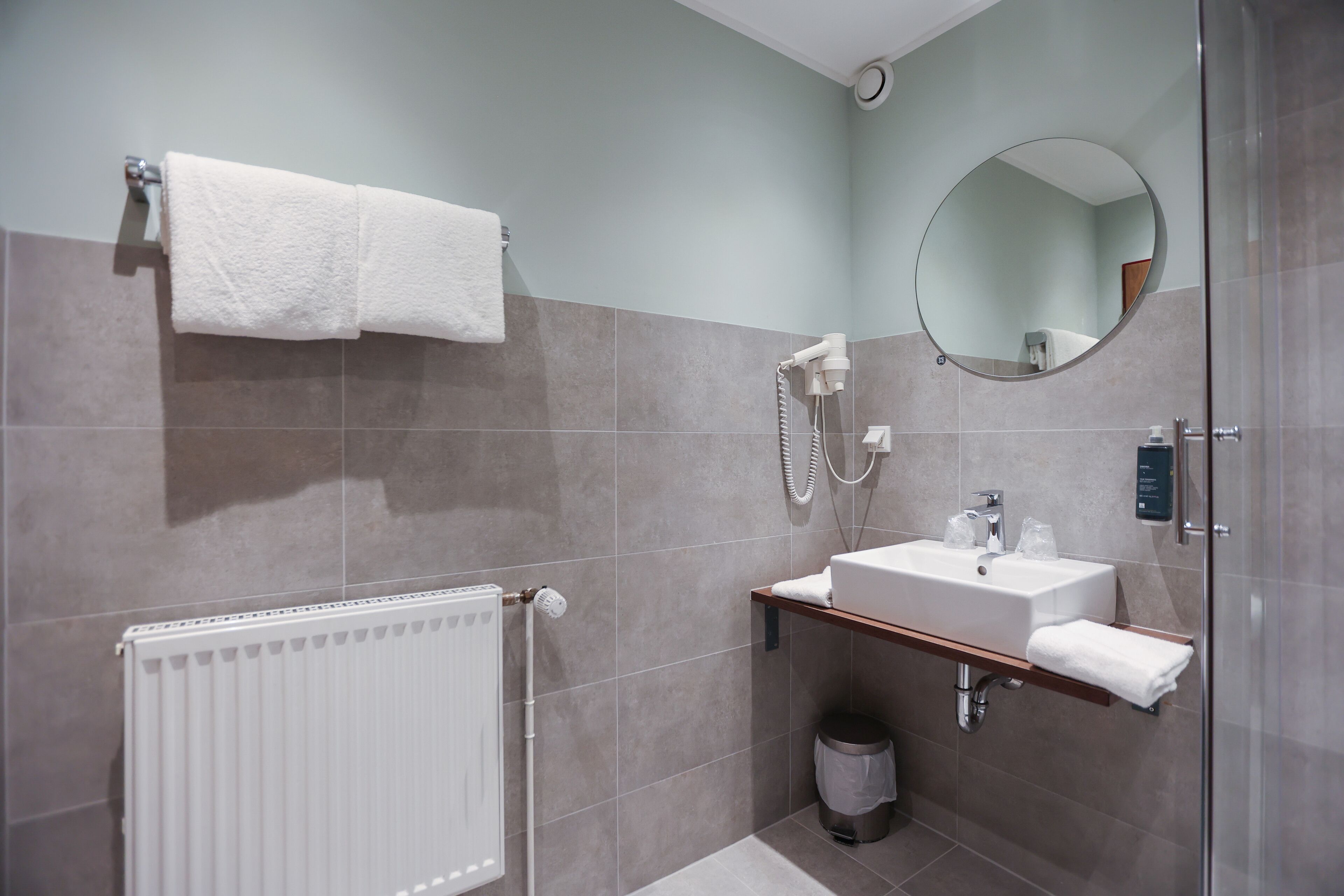 A modern bathroom with a white radiator, a glass shower enclosure, a sink with a mirror, and a towel rack.