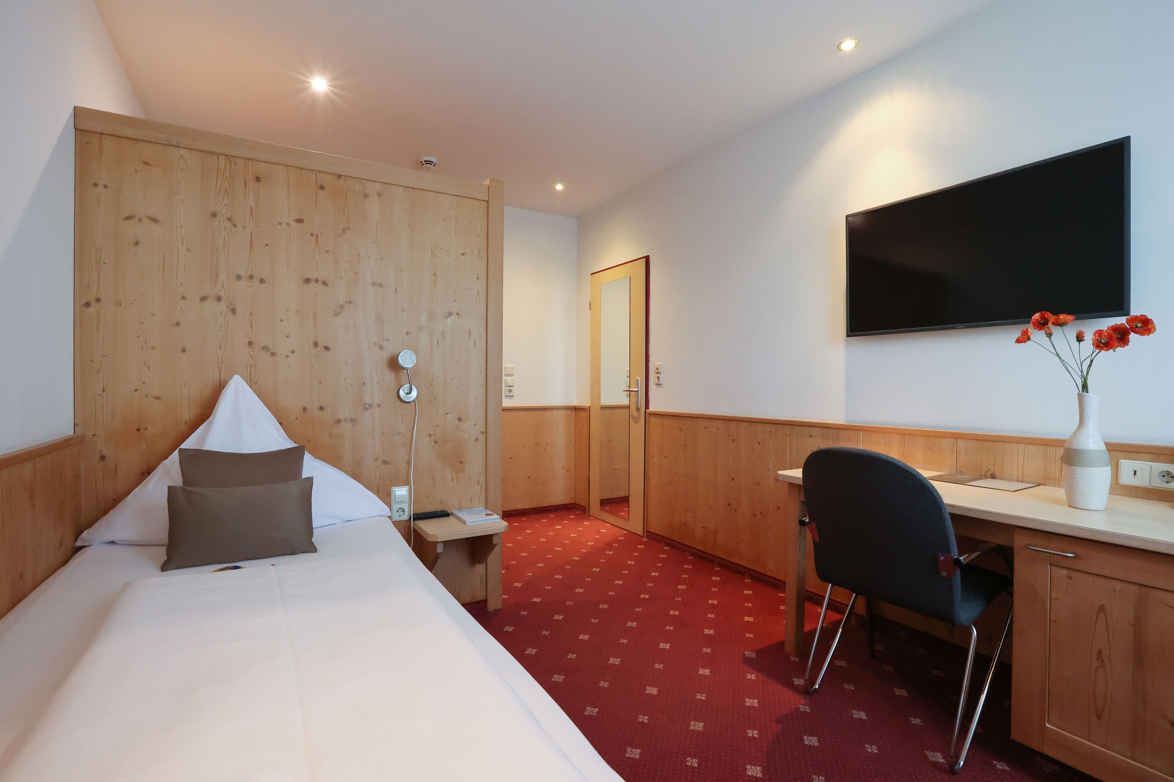 Een hotelkamer met een bed, een bureau, een stoel, een spiegel en een televisie aan de muur.