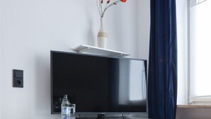 A modern room with a white desk, a flat-screen TV, a vase with flowers, and a radiator. - Arthotel ANA Panorama, Trademark Collection by Wyndham (Marktoberdorf)