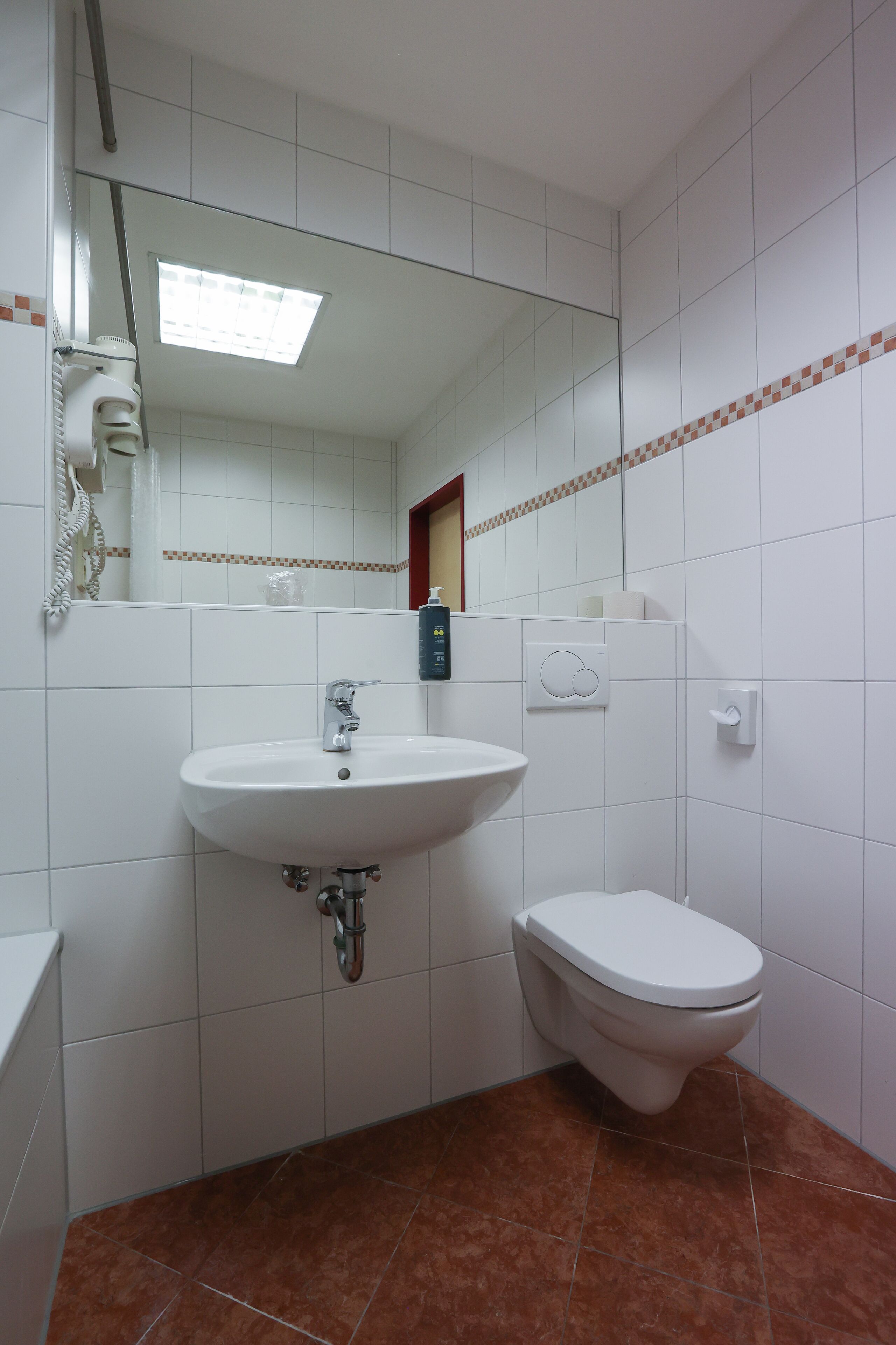 Un baño con azulejos blancos, un lavabo, un inodoro y un espejo.