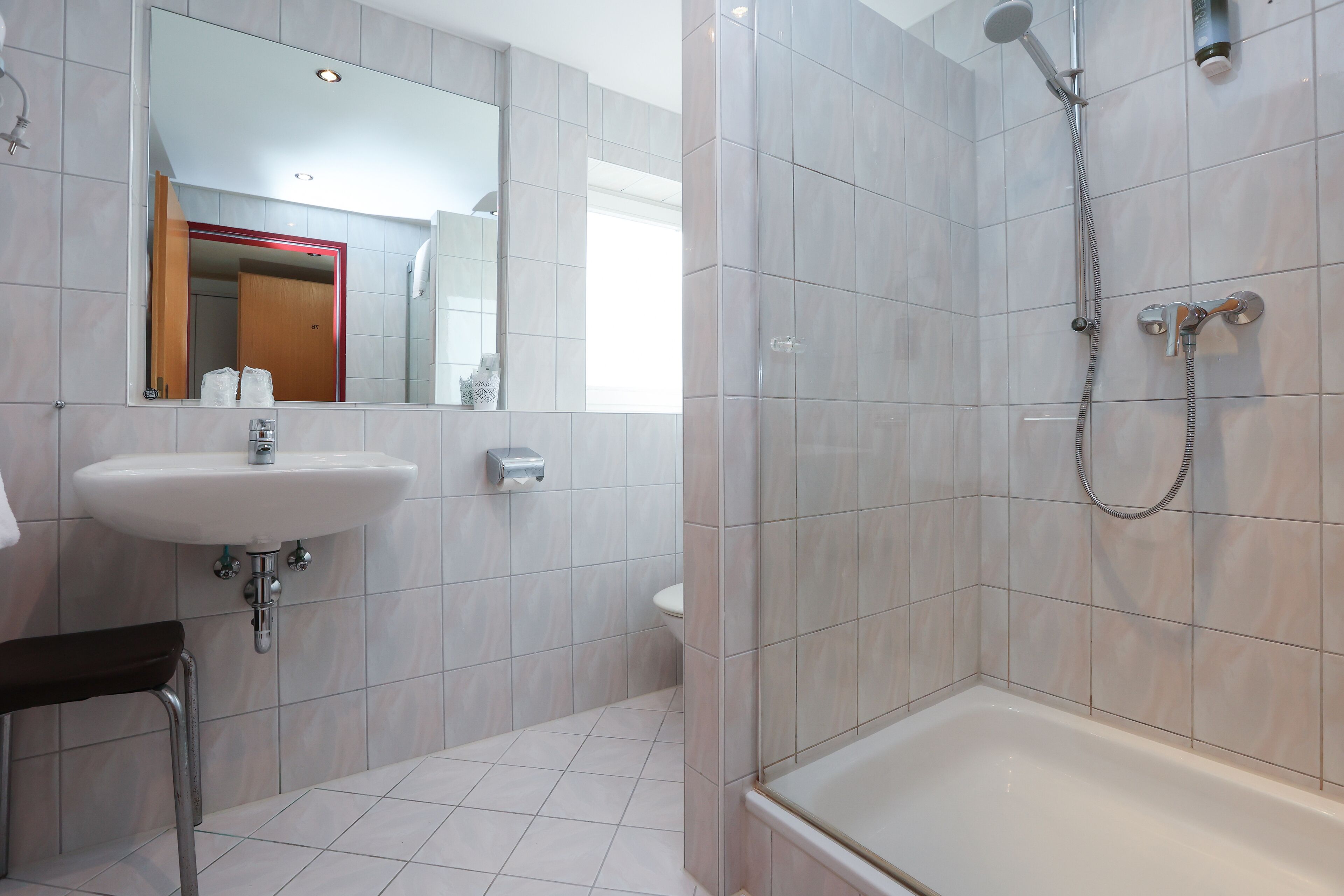 A modern bathroom with a white sink, a mirror, a shower area, and a bathtub.