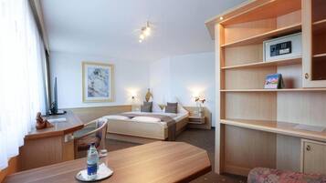 Una habitación de hotel con cama, mesitas de noche, escritorio, silla, sofá, estantería y un cuadro en la pared.
