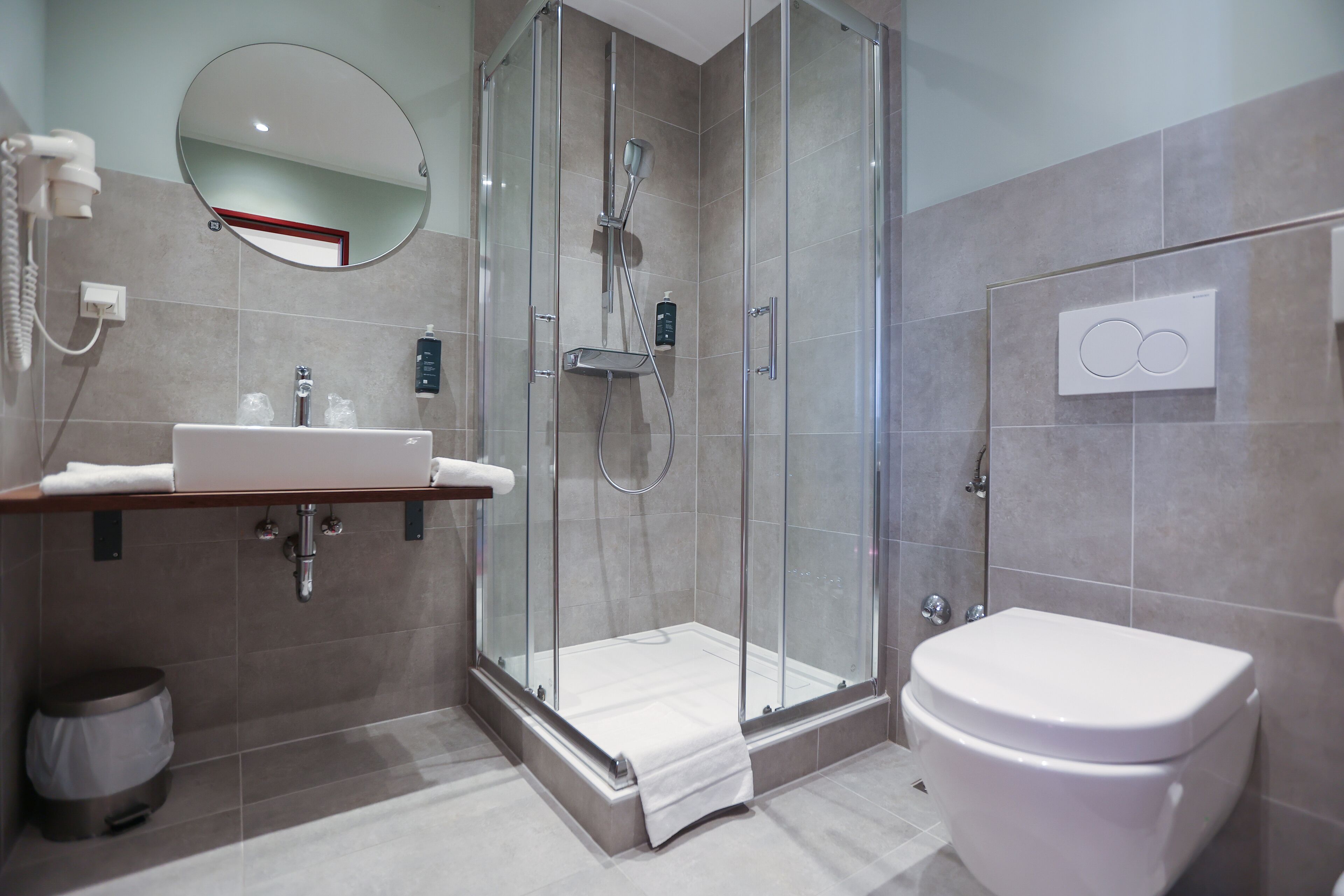 Un baño moderno con ducha de vidrio, lavamanos con espejo y retrete.