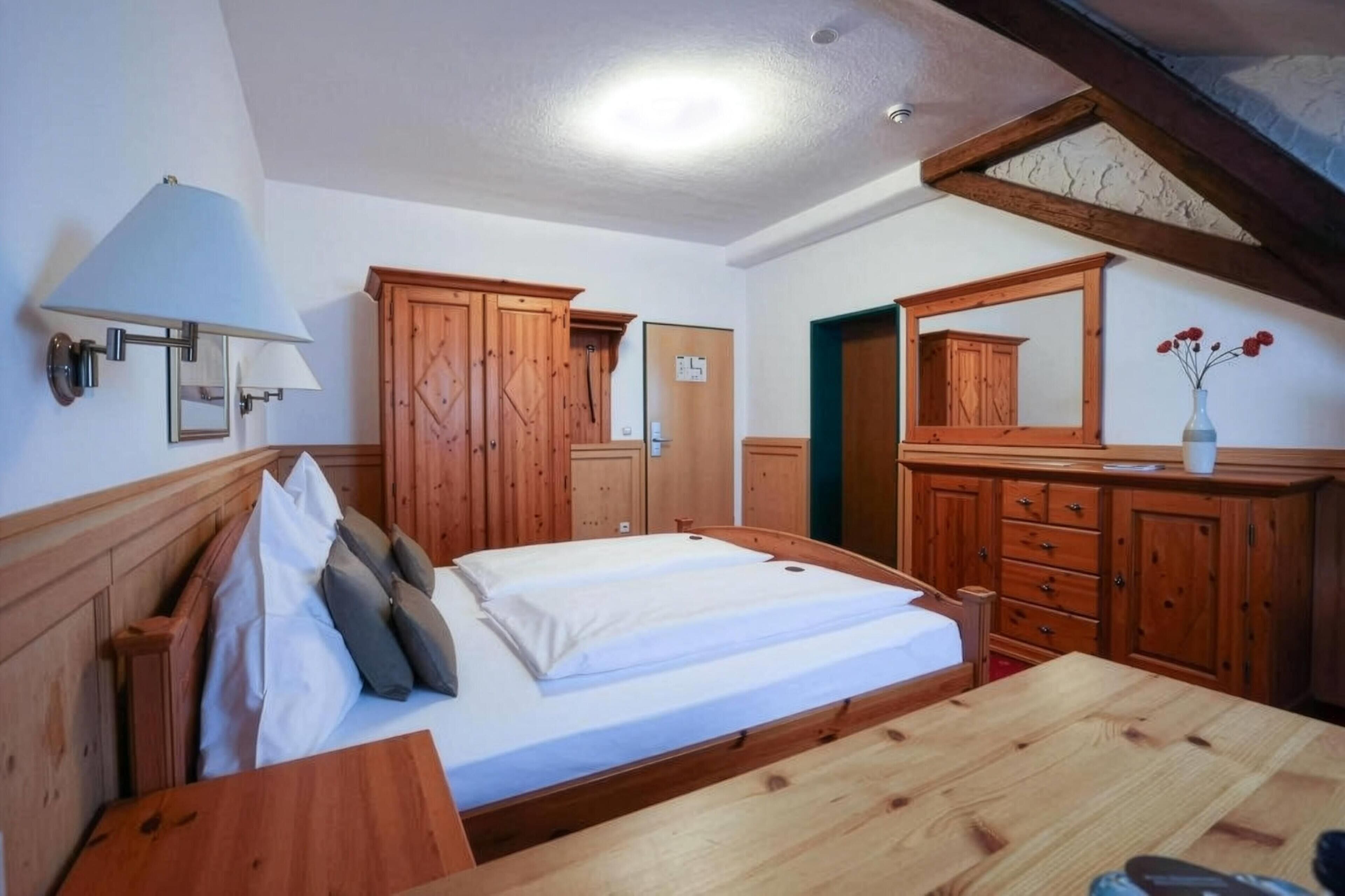 Een kamer met een bed, een houten garderobe en een spiegel.