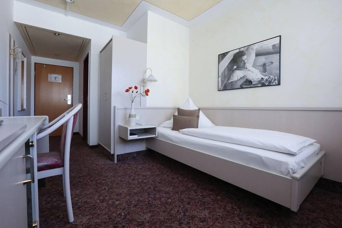 A hotel room with a bed, a desk, a chair, a nightstand, a lamp, and a framed picture on the wall.