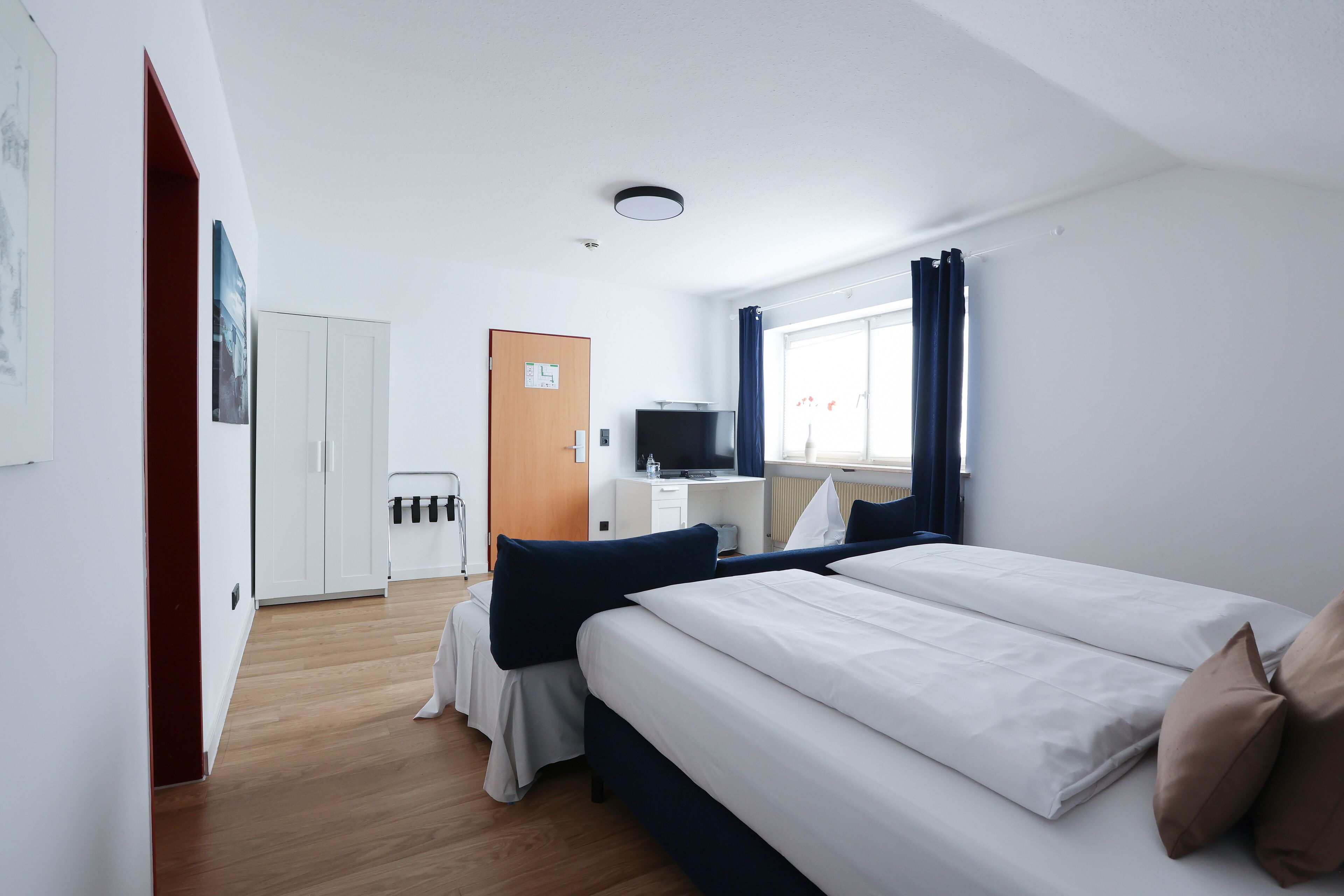 A modern hotel room with a large bed, a desk with a computer, a television, and a window with curtains.
